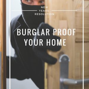 A burglar dressed in black clothes, black stocking cap, mask and gloves opening a wooden door with a metal doorknob.