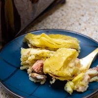 blue plaid plate next to a brown casserole dish with scalloped potato pie with ham