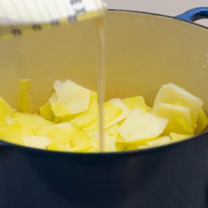 Stirring in cream and spices to a pot of boiled sliced potatoes