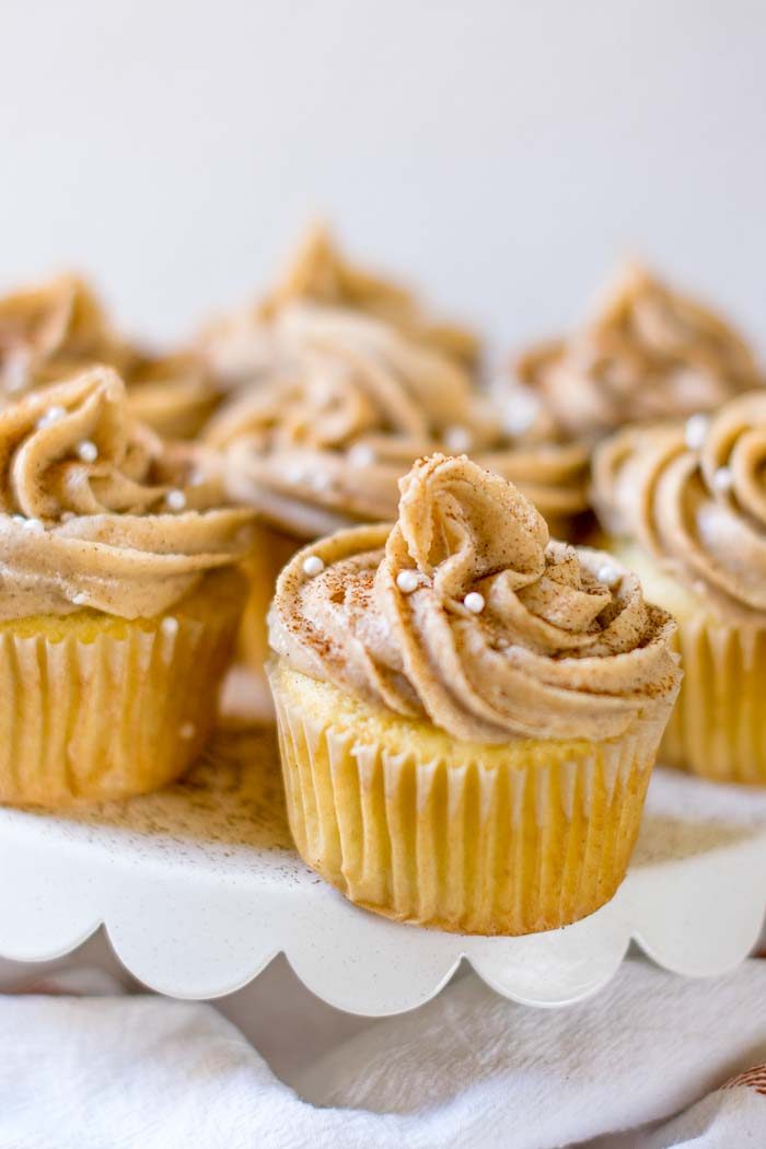 Snickerdoodle cupcakes with maple frosting on a scalloped white cake plate