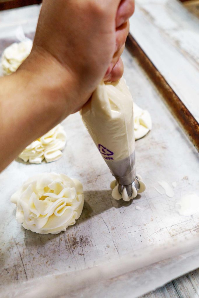 a russian piping tip is used to pipe stabilized whip cream frosting directly onto wax paper from a disposable piping bag