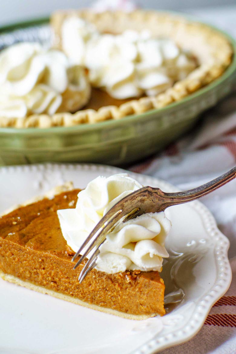 A fork full of molasses pumpkin pie on a dinner table set for thanksgiving
