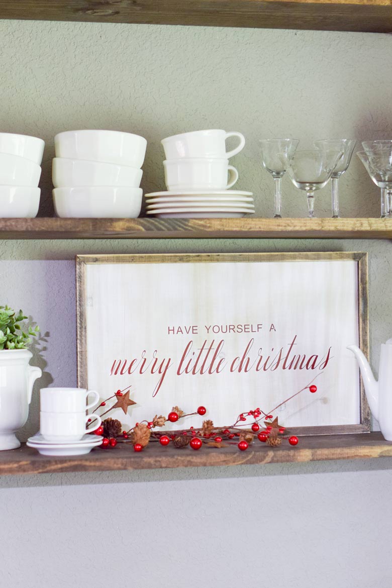 a rustic farmhouse sign on wooden shelves for a Christmas holiday display with white dishes
