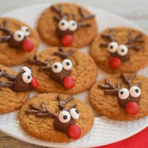 Gingerbread reindeer cookies on a white plate with faces made from chocolate kiss candy, candy eyes and a candy nose.