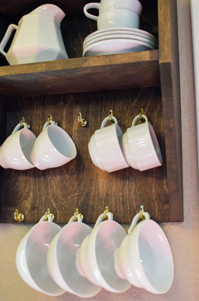 espresso cups hanging from gold cup hooks on a wooden wall rack for mugs