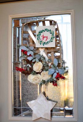 A winter wreath made from white roses, evergreens, berries and more on a tobacco basket hanging on a door.