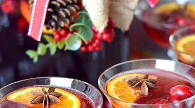 Two vintage coupe champagne glasses full of red cranberry juice and gingerale with floating cranberries, star anise and orange slice halves.