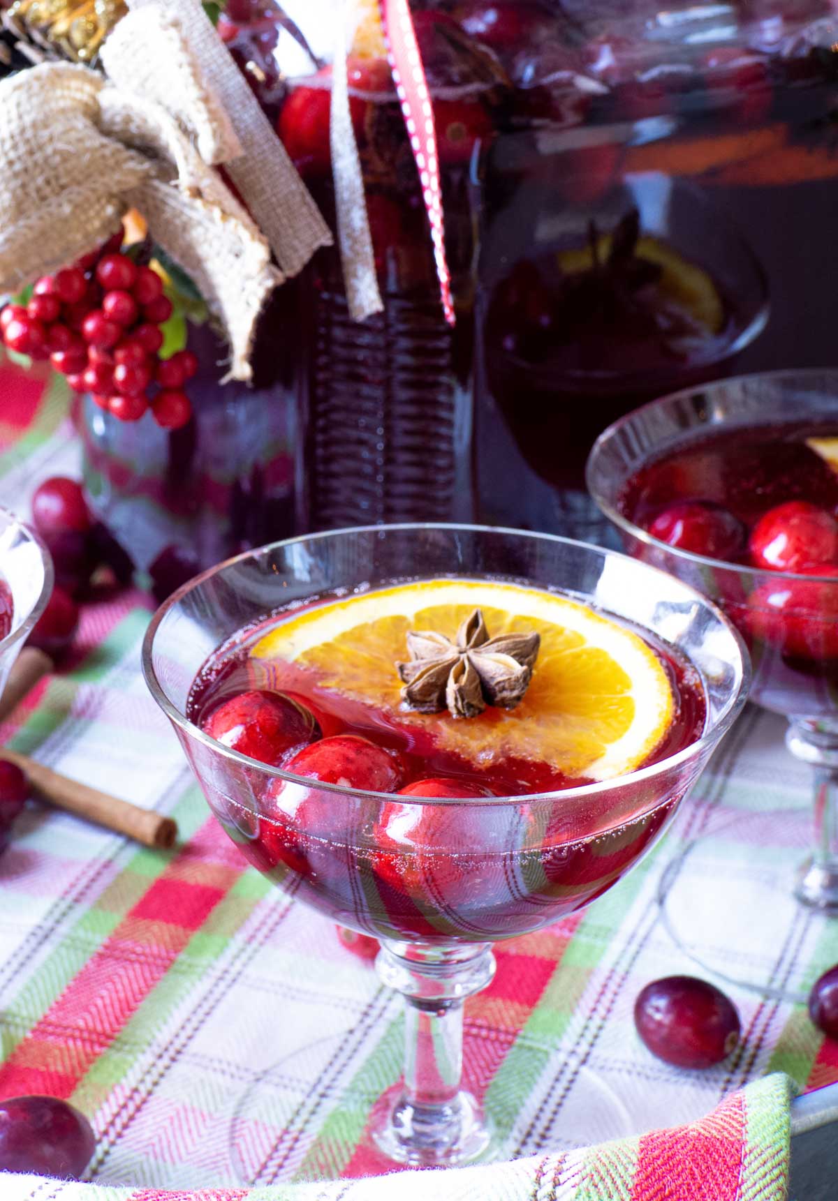 A star anise spice sits atop an orange slice in a cranberry holiday beverage served in a champagne glass