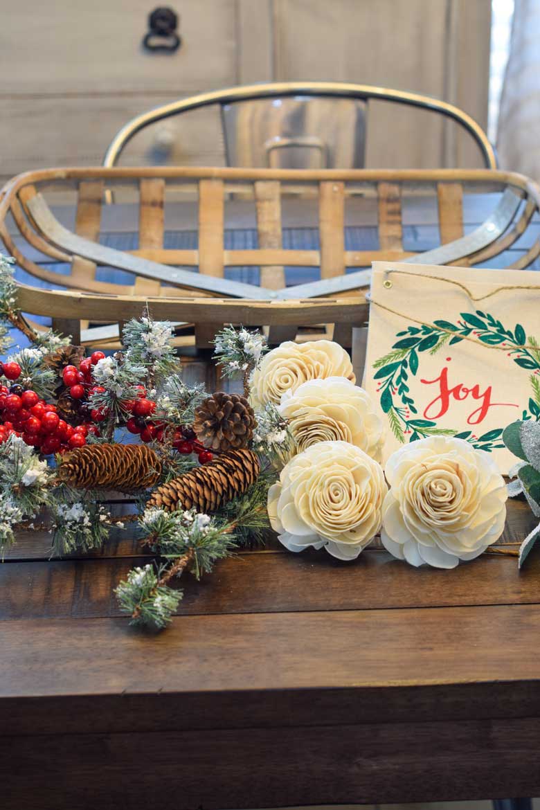 Supplies needed for a winter front door wreath includes rose stems, evergreen floral picks with berries, a tobacco basket, and more