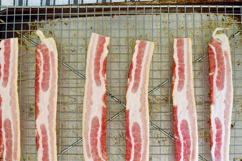bacon lined up on a rack over a cookie pan about to go in the oven