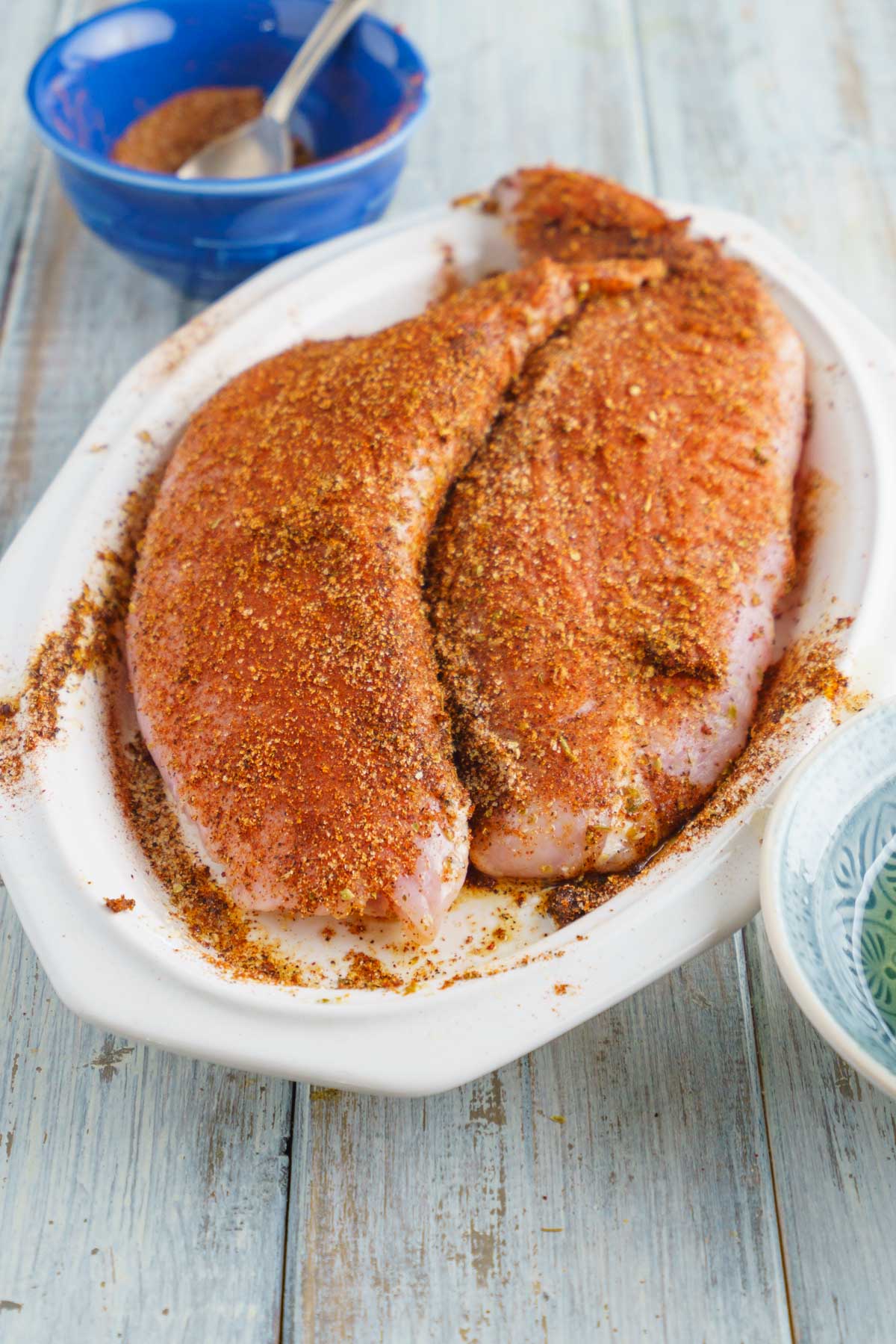 a white platter with large turkey breast tenderloins coated in a spice rub.