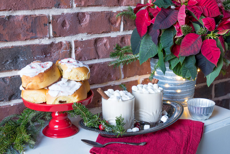 white cocoa on a table with cinnamon rolls and a poinsetta