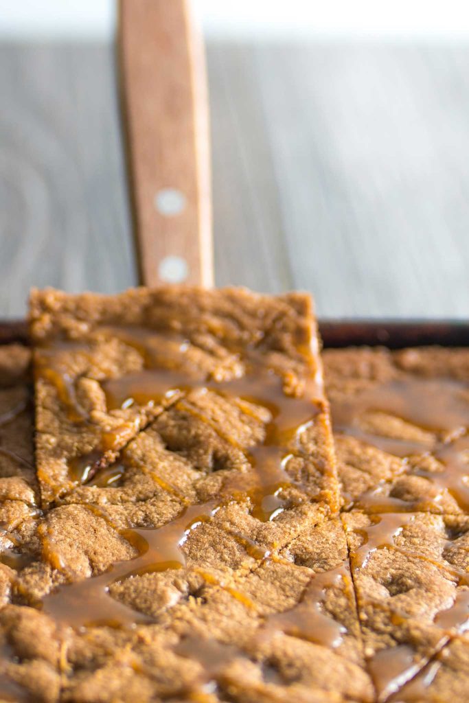 dense and crispy cookie bars in a sheet pan being lifted up by a spatula