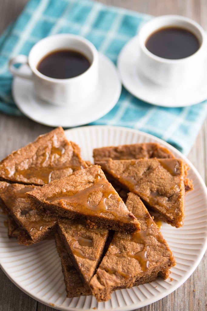 crispy chocolate chip cookie bars with caramel bits on a white plate with two cups of espresso