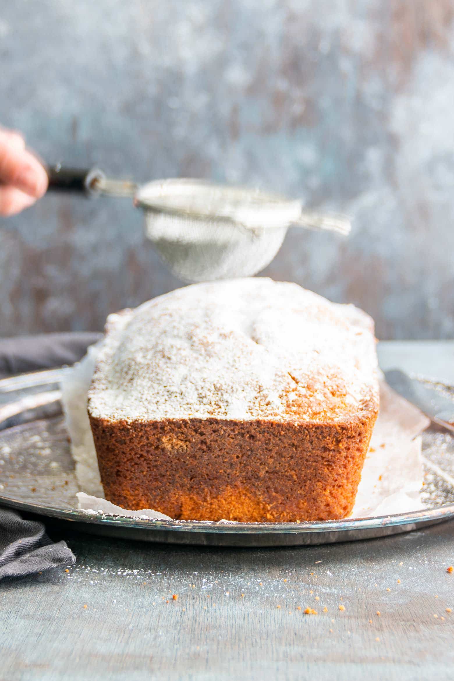 dusting powdered sugar on an autumn spice loaf cake