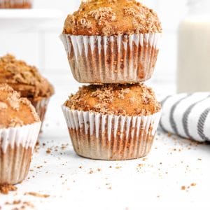 two stacked oatmeal banana muffins with white liners next to a towel
