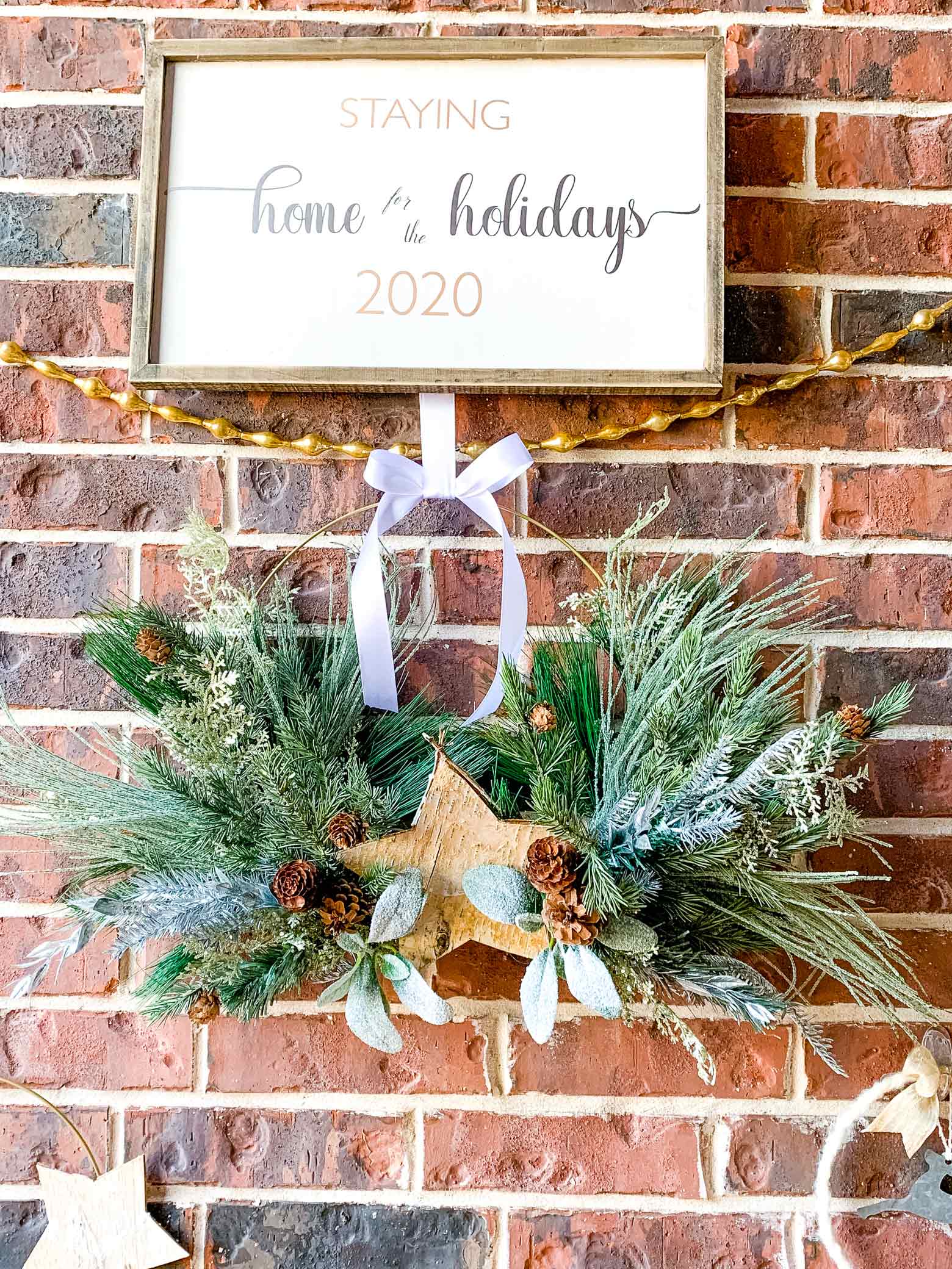 wooden Christmas sign above gold garland and a wreath with greenery
