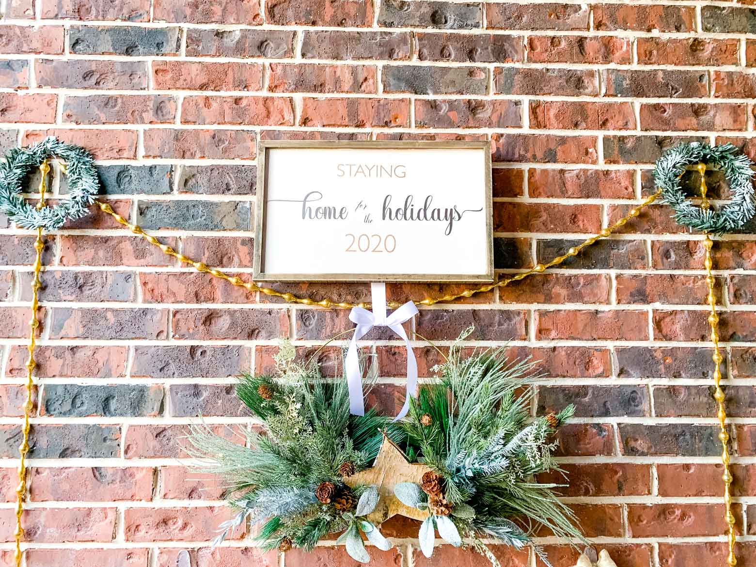 two small green wreaths and gold garland flank a holiday sign