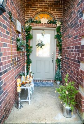 A bench on front porch with a wall of wreaths and a garland covered from door.
