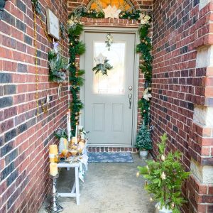 A bench on front porch with a wall of wreaths and a garland covered from door.