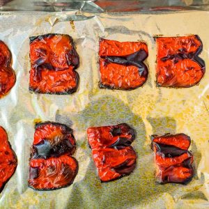 roasted red pepper pieces after being roasted on a sheet pan topped with aluminum foil