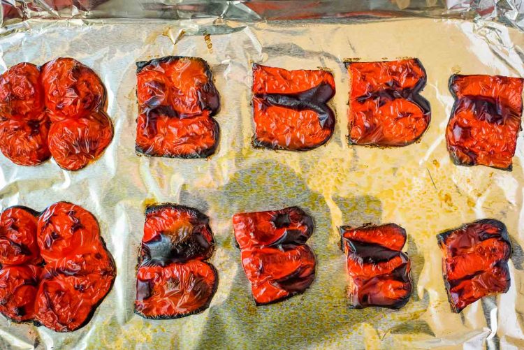 roasted red pepper pieces after being roasted on a sheet pan topped with aluminum foil