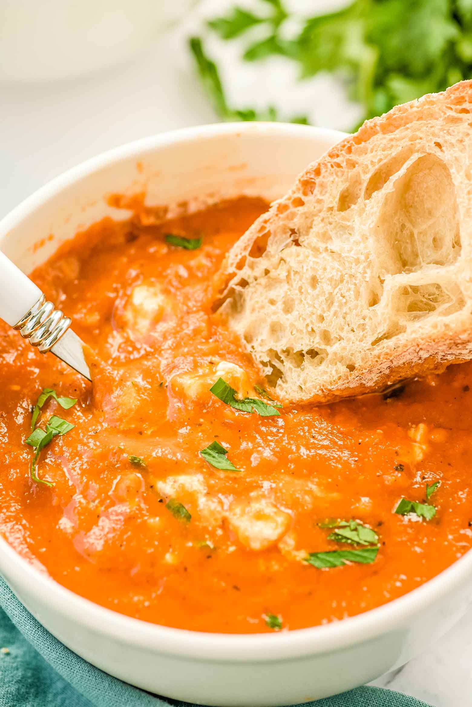 dipping bread into a hearty soup in a white bowl and fresh Italian parsley