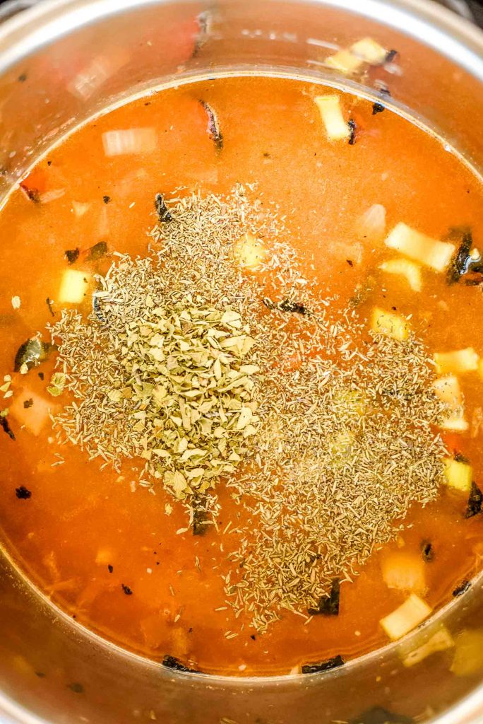 dried herbs on top of a chunky soup in a pressure cooker