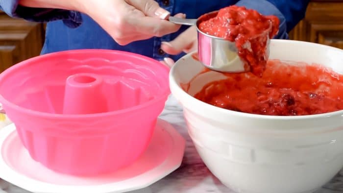 Ladling unset cranberry jello salad into a pink bundt cake shape mold.