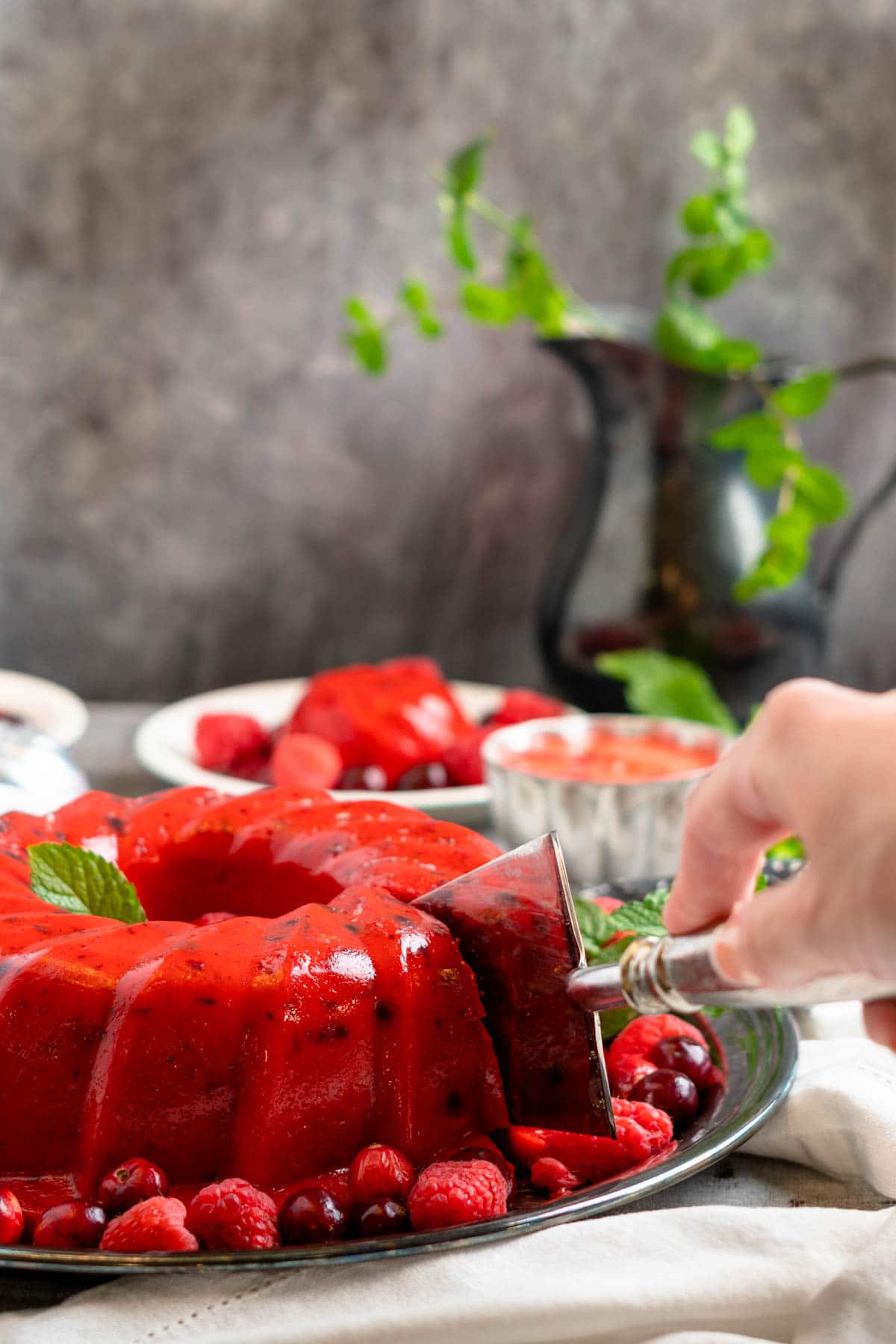 A silver cake slicer cutting into a red jello circle ring on a platter. 