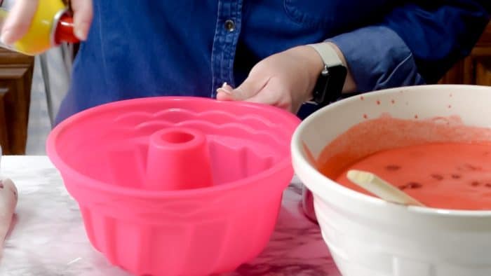Spraying a pink silicone bundt pan with nonstick baking spray