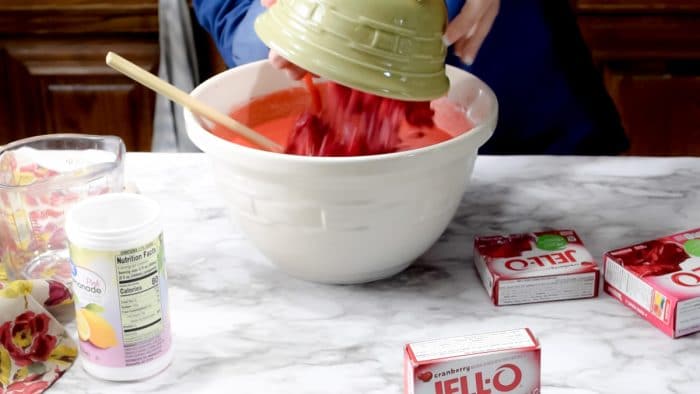 a green bowl of frozen berries being poured into a white bowl of jello being prepared.