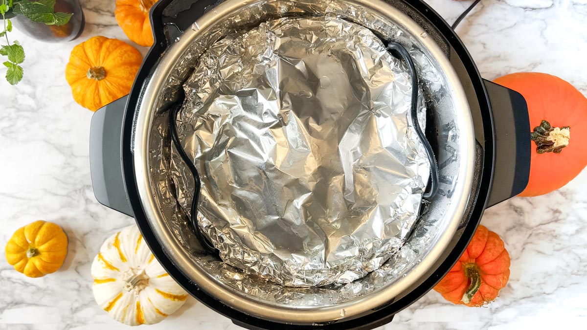 aluminum foil covered pan in an instant pot next to pumpkins.