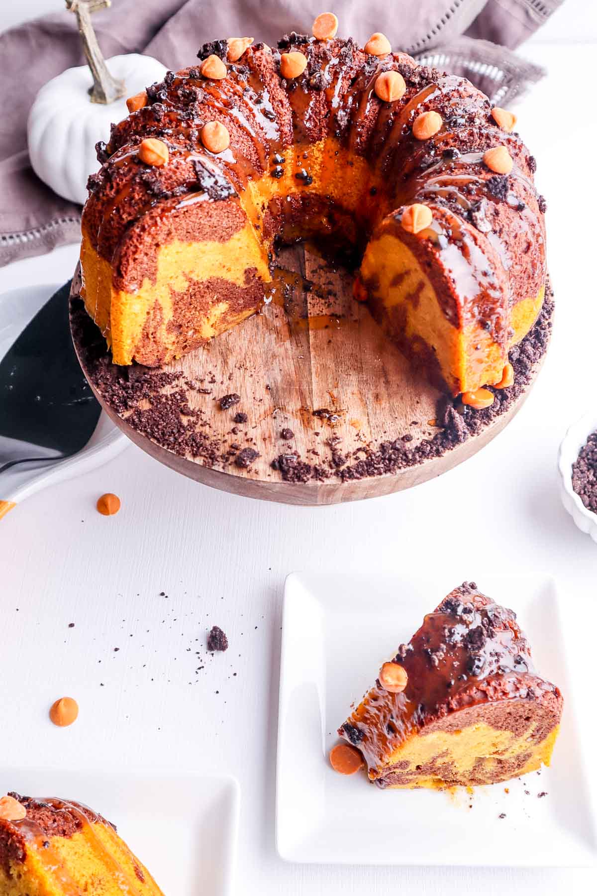 a chocolate pumpkin marbled bundt cake on a wooden cake stand with crushed oreo cookies. 
