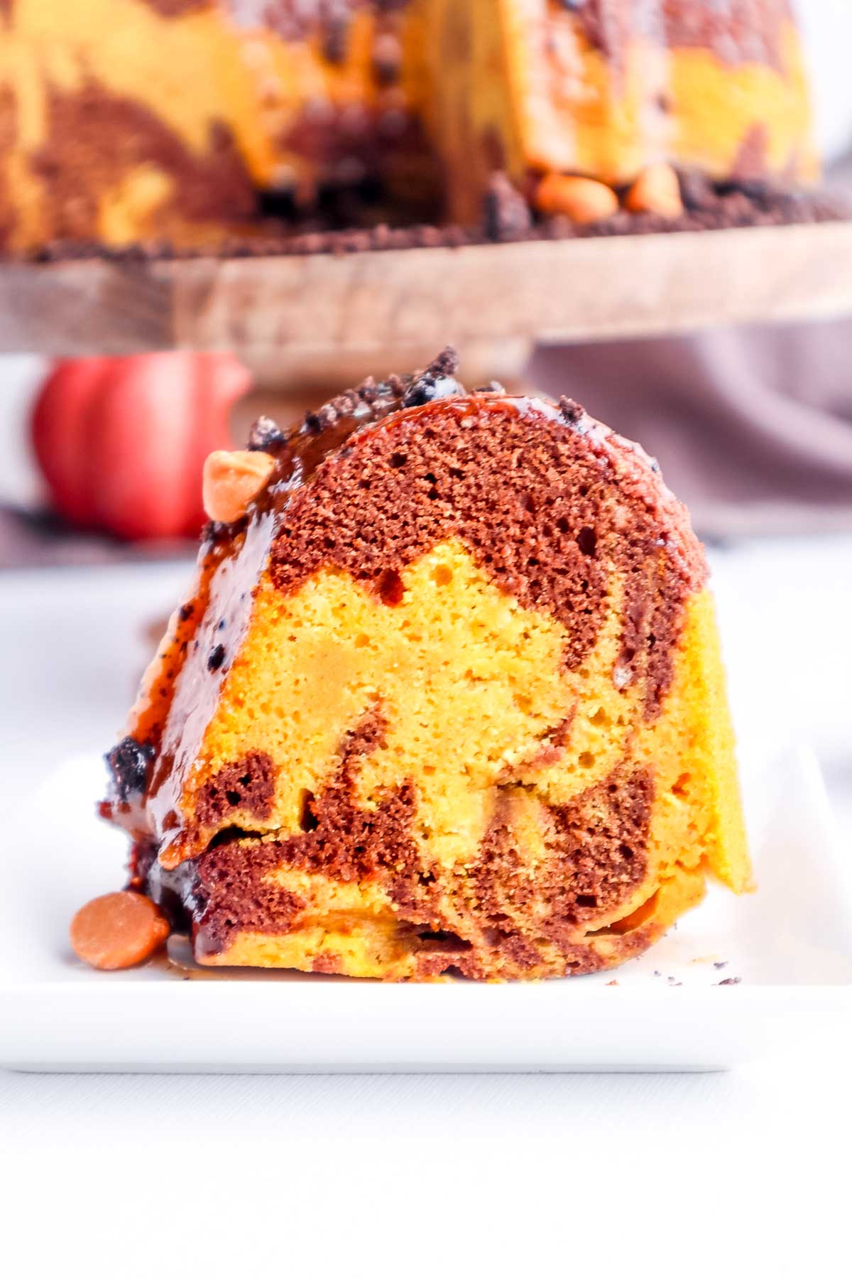 Close up shot of a swirled pumpkin and chocolate slice of bundt cake on a white plate.