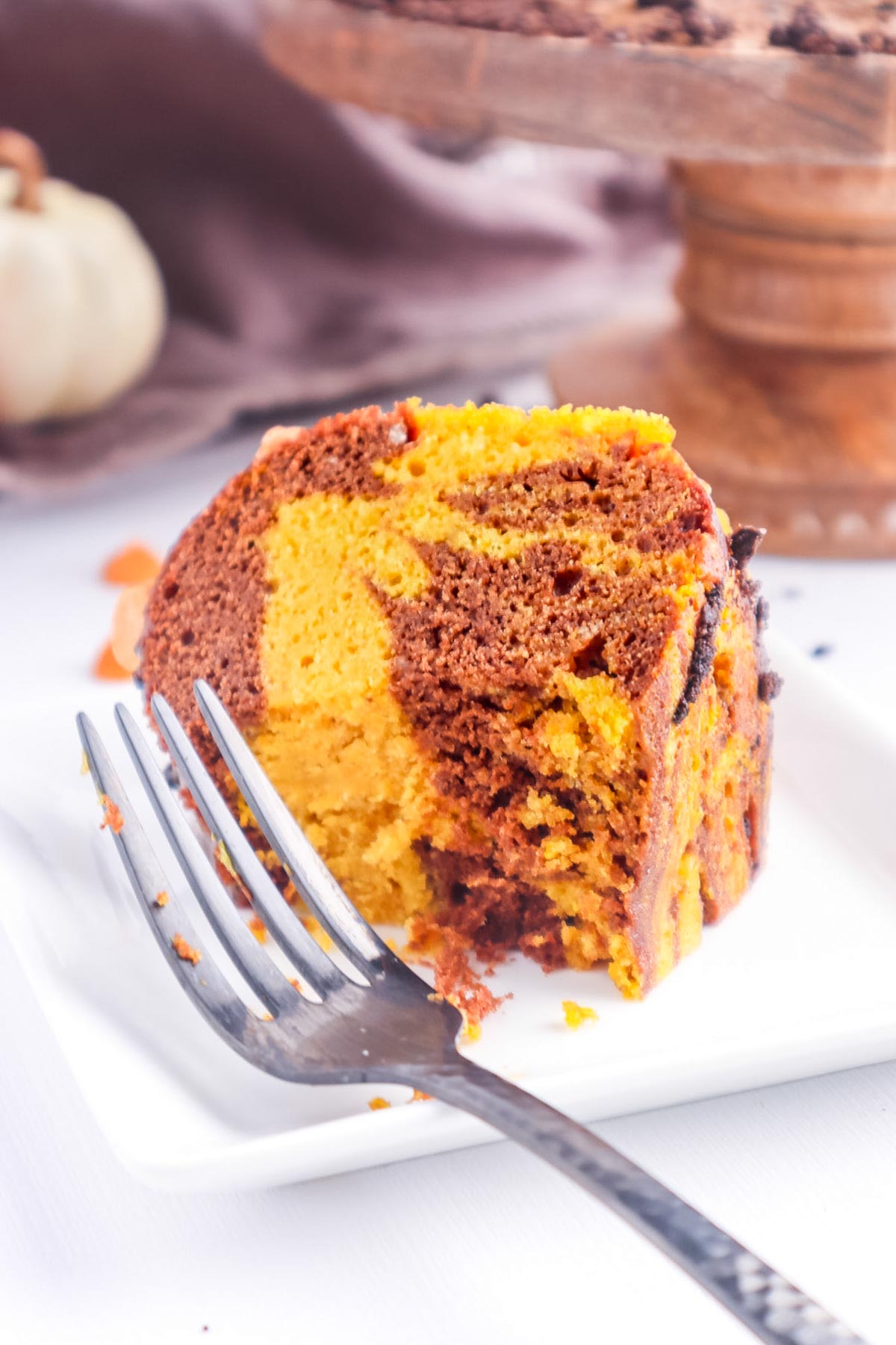 an orange and cocoa colored swirl cake piece on a white plate with a fork. 