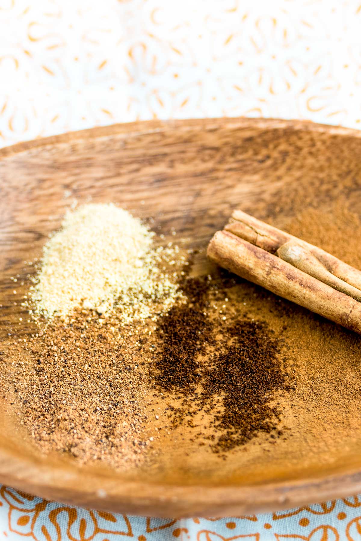 a wooden plate with a cinnamon stick and dustings of ginger, nutmeg and dark ground cloves. 