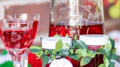 Cranberry vodka in bottles and glasses and small jars on a tray.