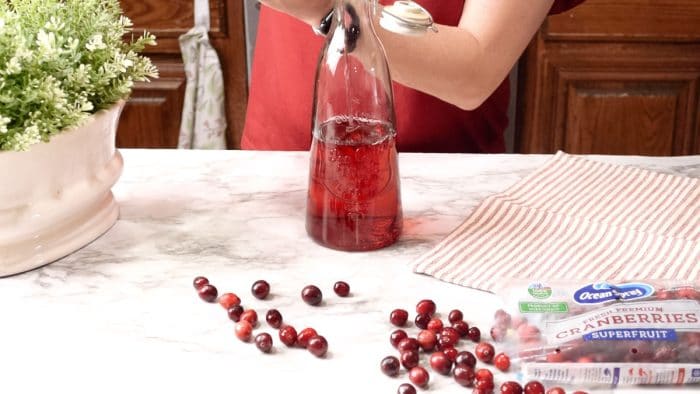 Funneling homemade cranberry vodka into a tall glass bottle with a ceramic lid.