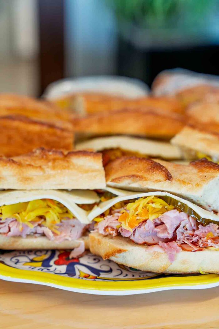 a platter of sandwiches with crispy bread filled with: smoked meat, fermented garlic flower mayo, sauerkraut, and short-fermented dill pickles
