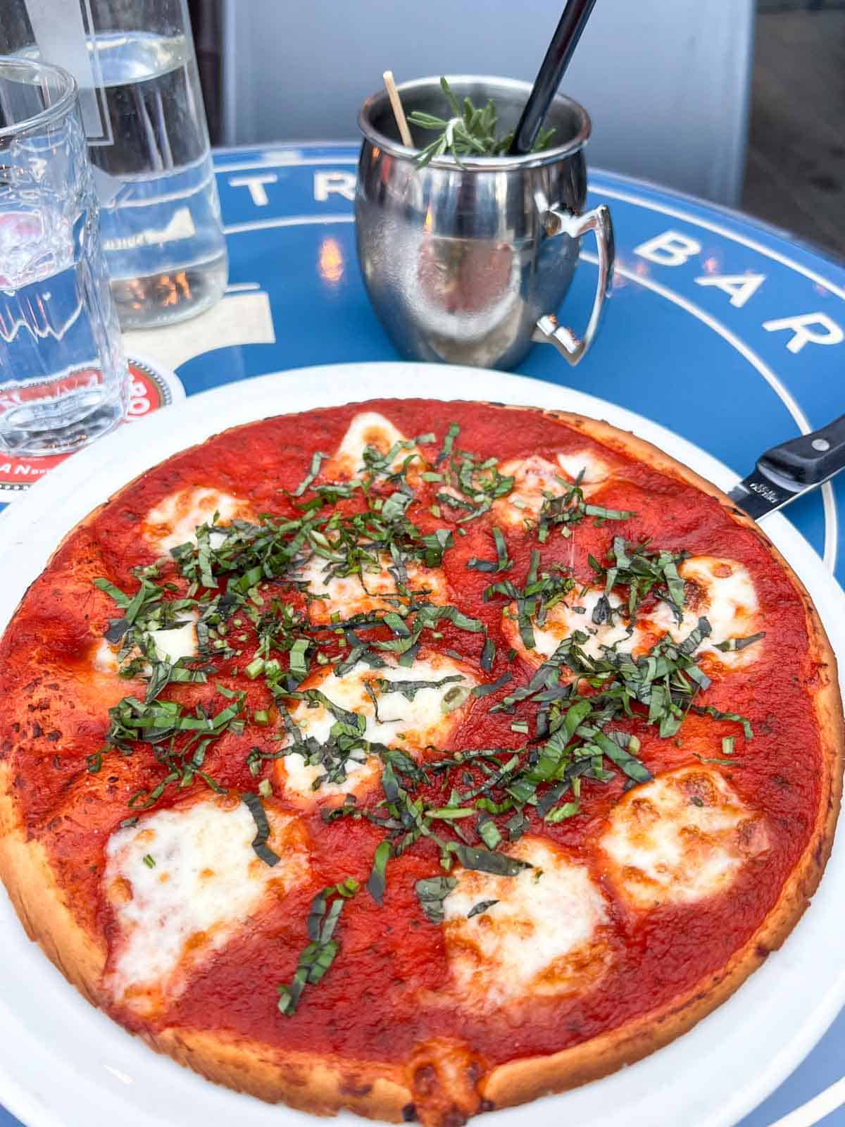a cauliflower crust margherita pizza next to a Moscow mule in a signature Moscow mule cup.