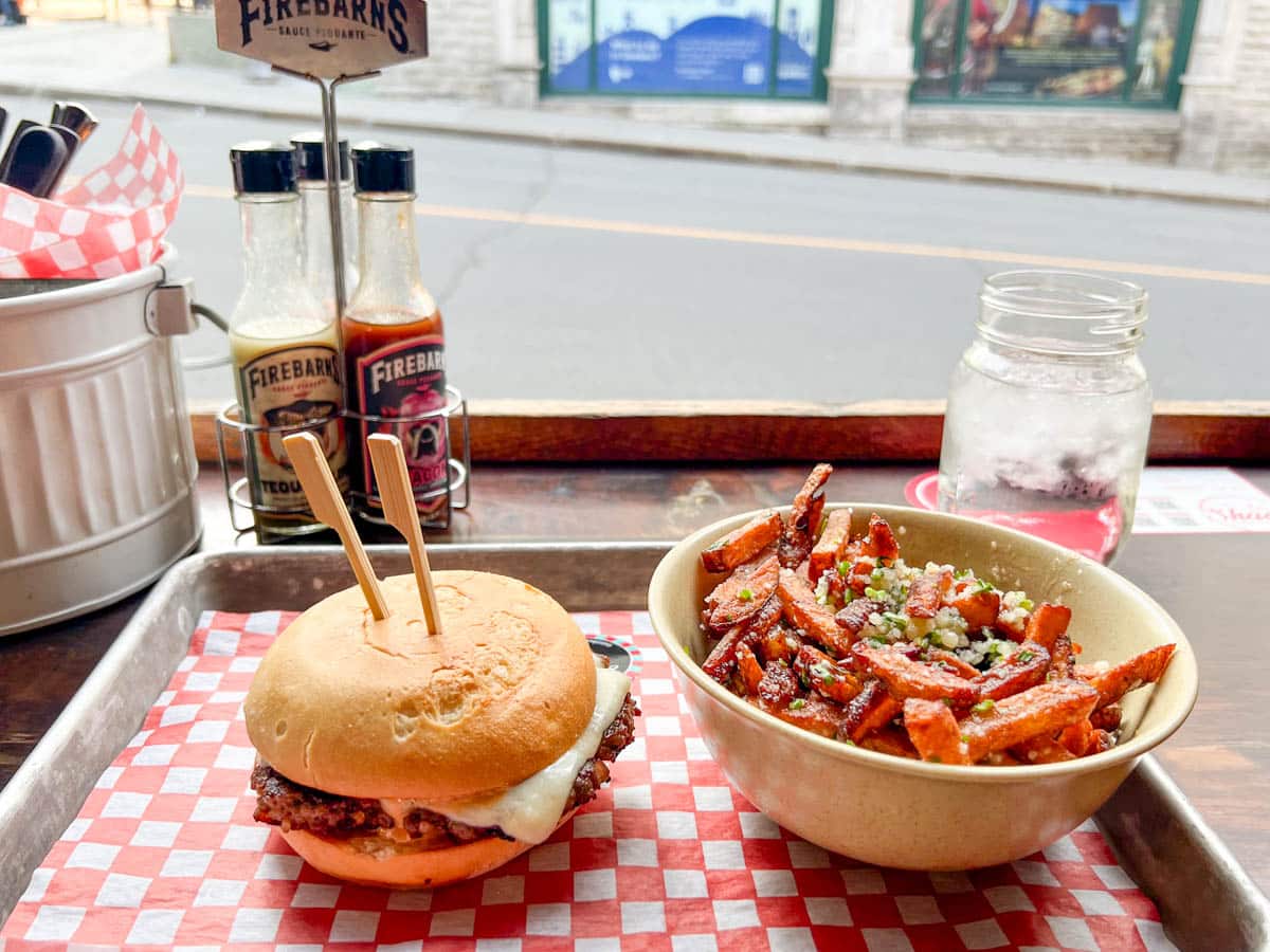 a cheeseburger next to a bowl of truffle and garlic flavored fries on a table looking out to a street.