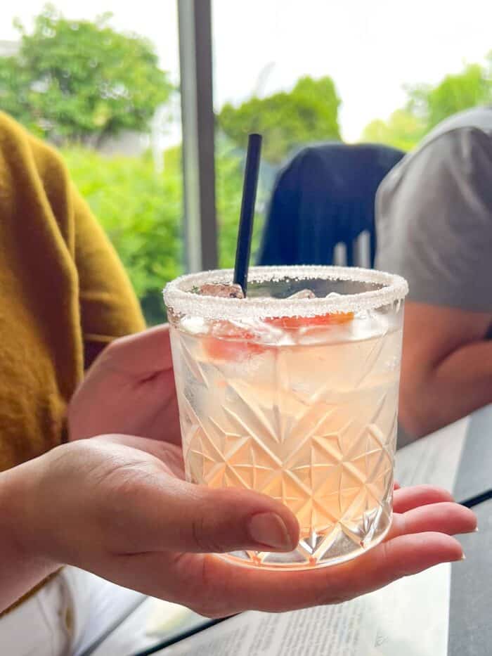 a glass tumbler containing an orange tinted grapefruit cocktail held in the hand of a woman.