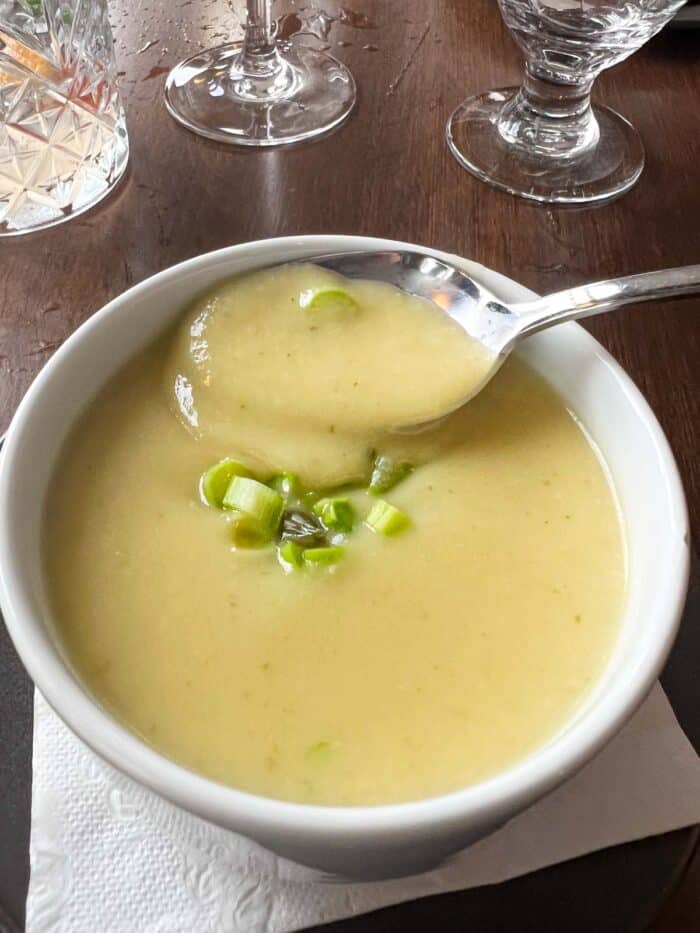 a white bowl containing a pureed vegetable soup of a yellowish color topped with green onions, and a spoon dipping into the bowl.