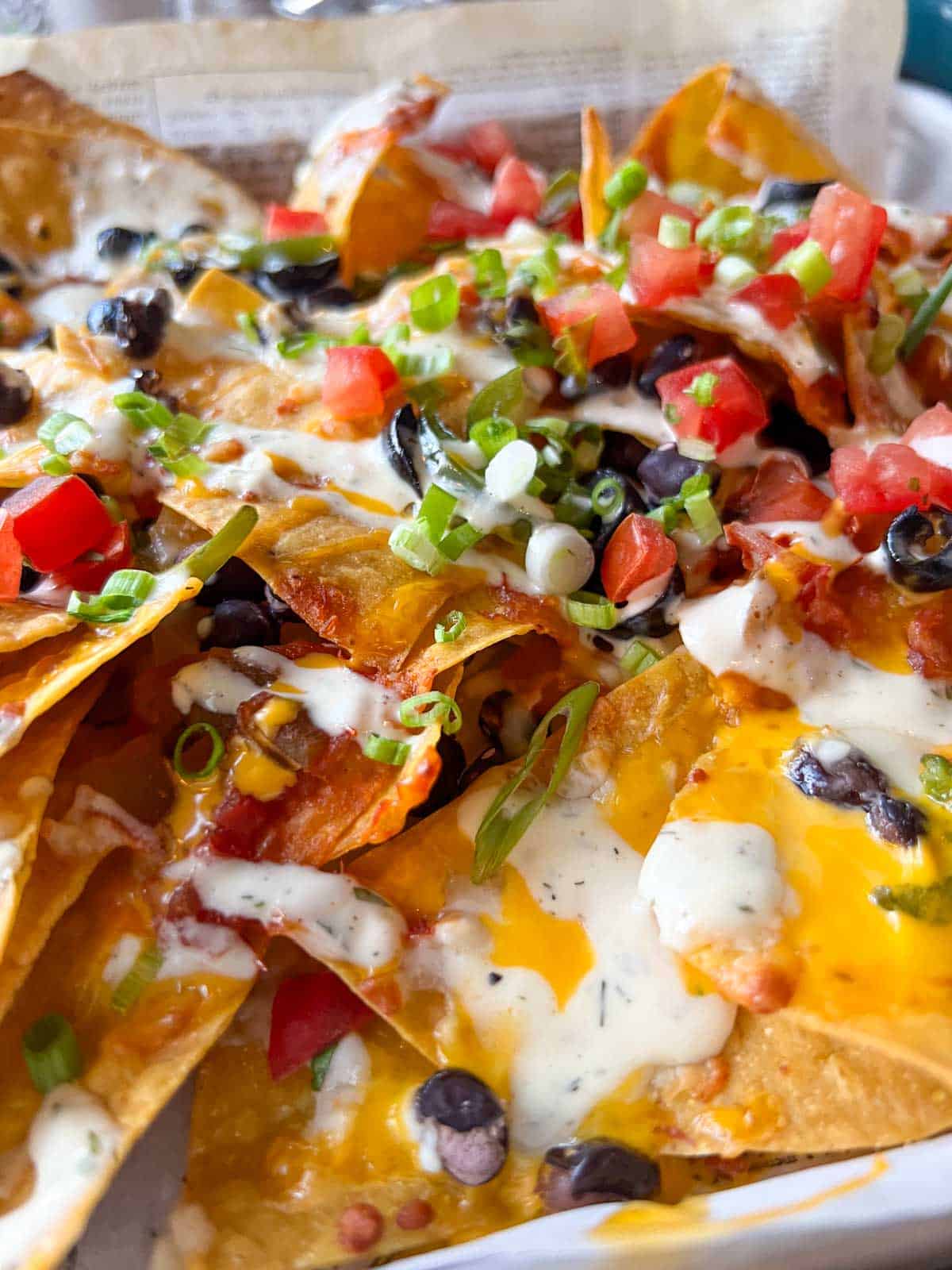 a tray of nachos: tortilla chips topped with cheese, black beans, olives, pico de gallo and ranch.