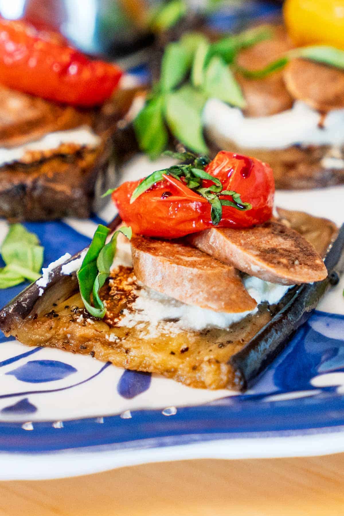 an eggplant appetizer with cherry tomatoes, lamb sausage, fresh cheese, and honey