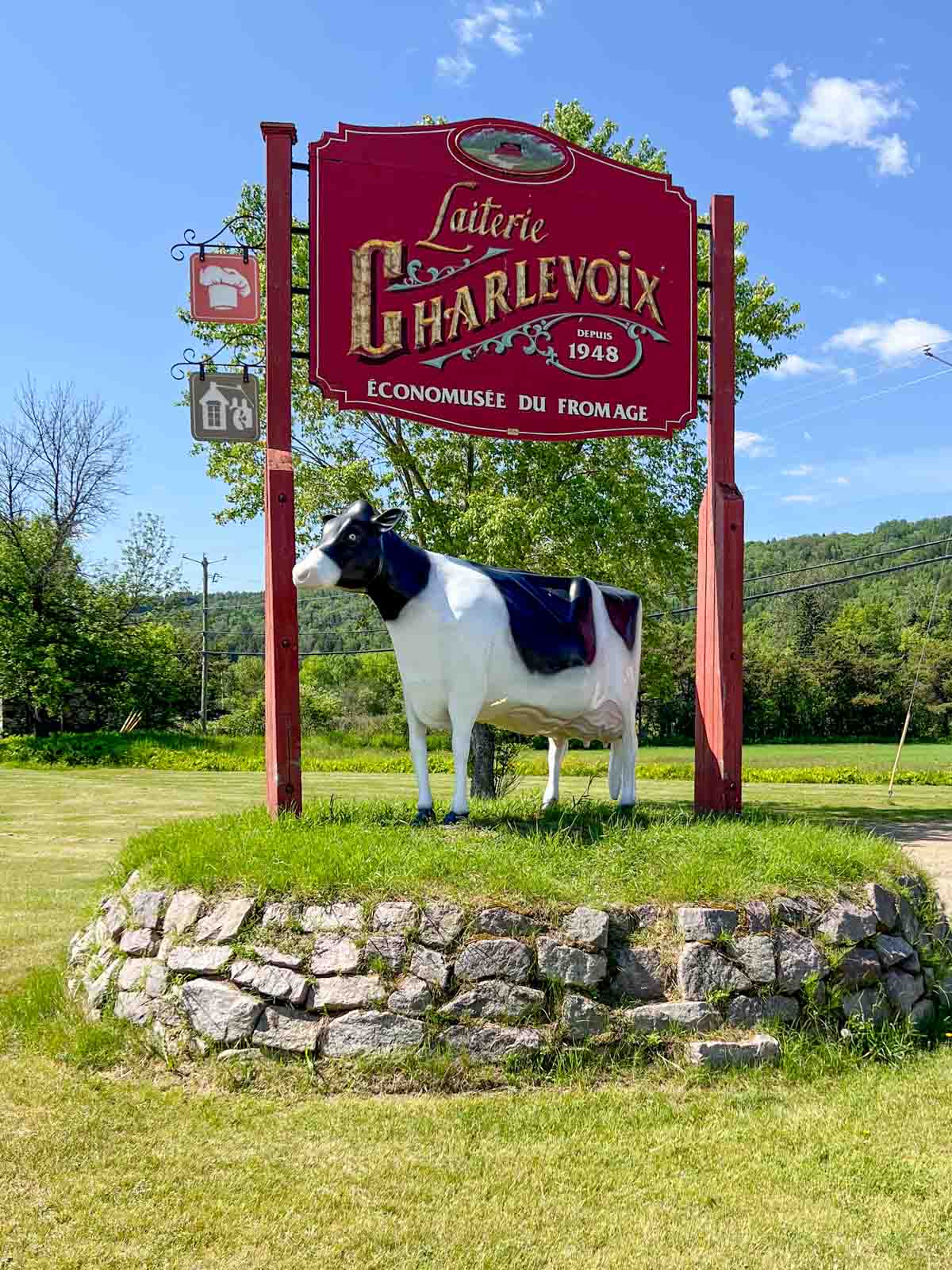 A red sign with the name Laiterie Charlevoix over a statue of a black and white cow.