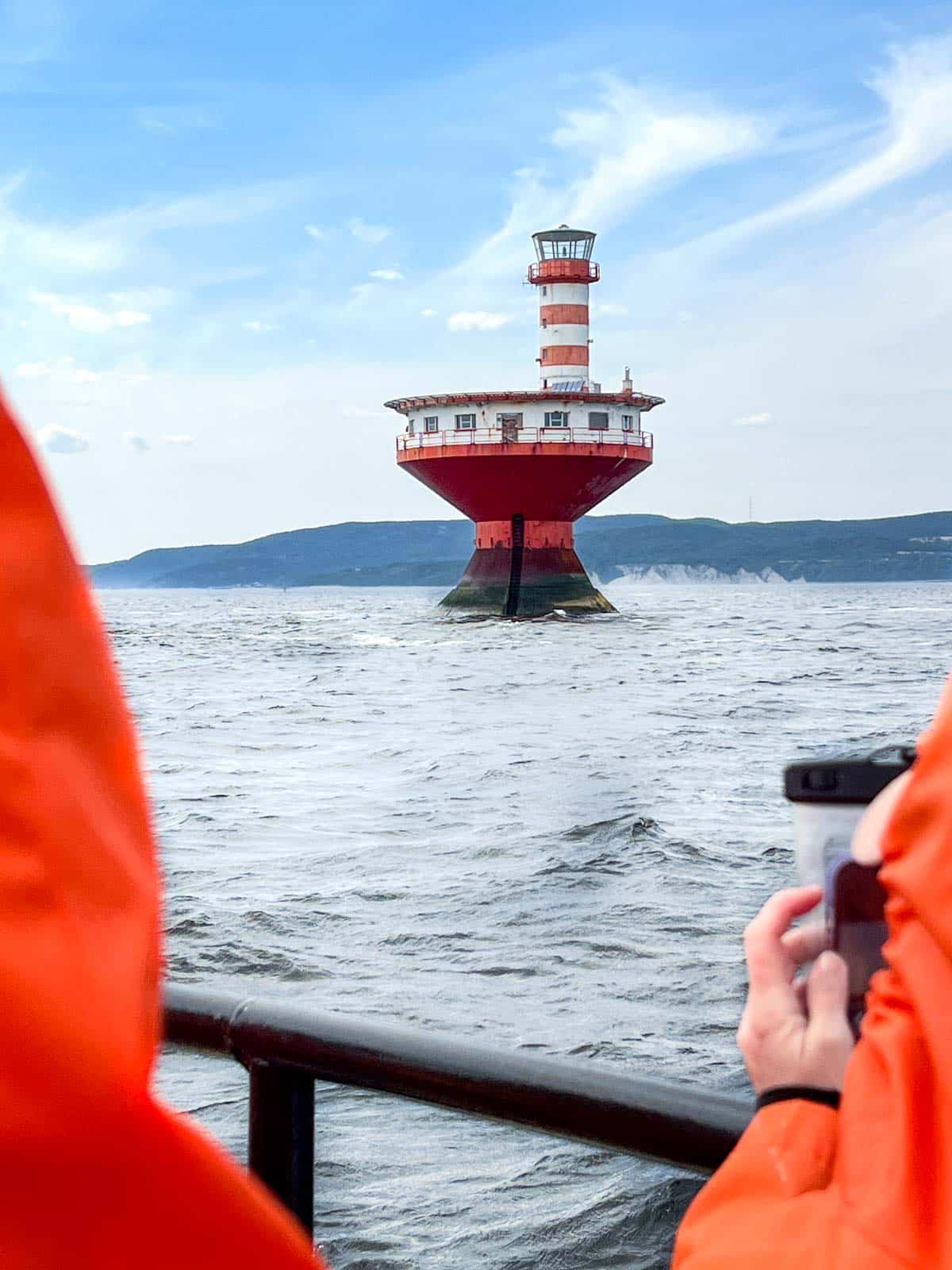 a red and white round lighthouse coming out of the water with hills in the background.
